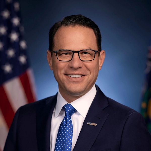 A man in a suit smiling with American flags in the background.