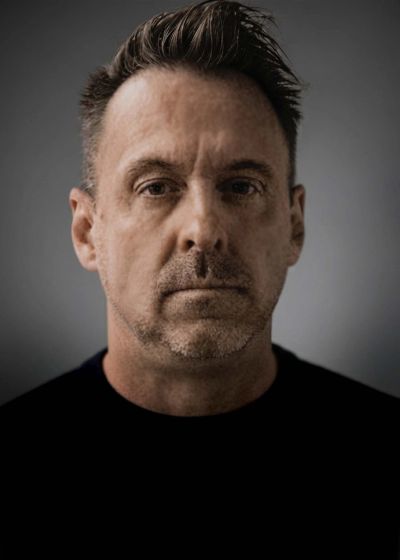 Serious middle-aged man with short hair and stubble.
