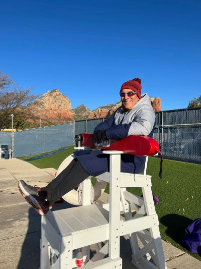 Man sitting on a lifeguard chair with a mountain backdrop.