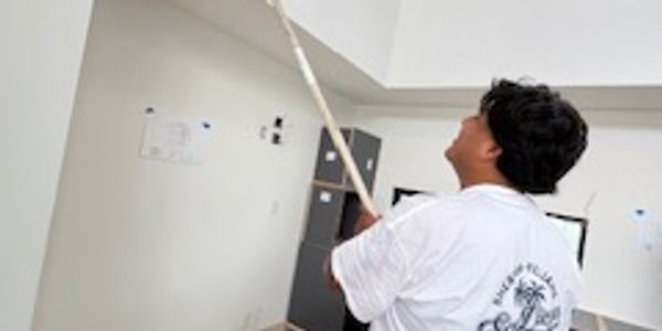 A man painting a high wall white with a roller.