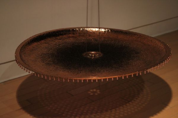 Hanging copper or bronze textured disc with small droplets around its edge.