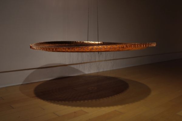 Suspended circular wooden sculpture casting a shadow.
