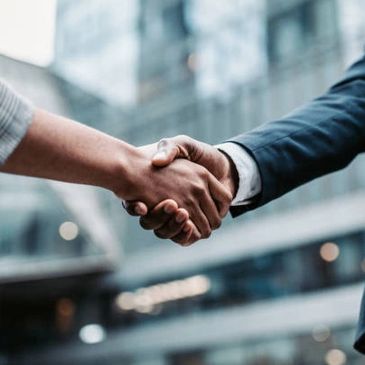 Two people shaking hands outside a modern office building.