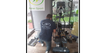 Técnico reparando una máquina elíptica en un gimnasio.