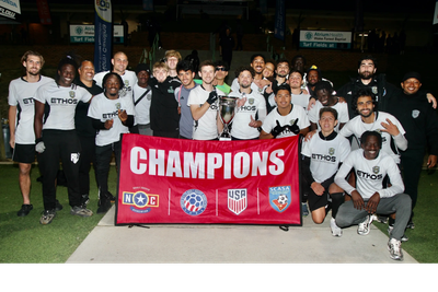 Soccer team celebrating championship victory with a large red "CHAMPIONS" banner.