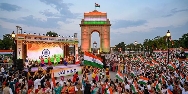 Crowd celebrates India's Independence Day at India Gate with flag waving and cultural performances.