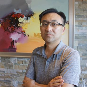 Man standing confidently with arms crossed in front of colorful abstract painting.