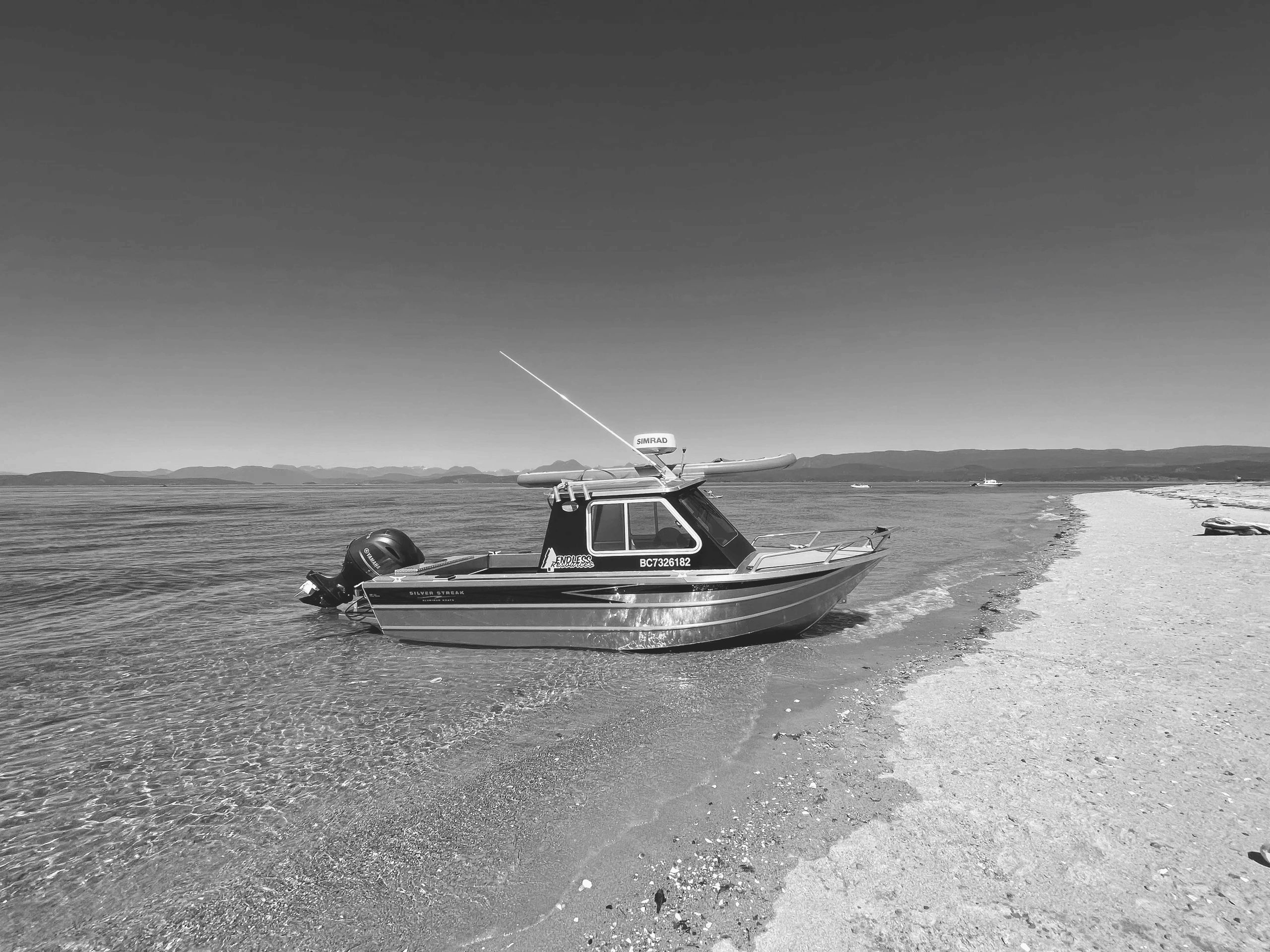 A small motorboat anchored on a clear sandy beach under a bright blue sky.