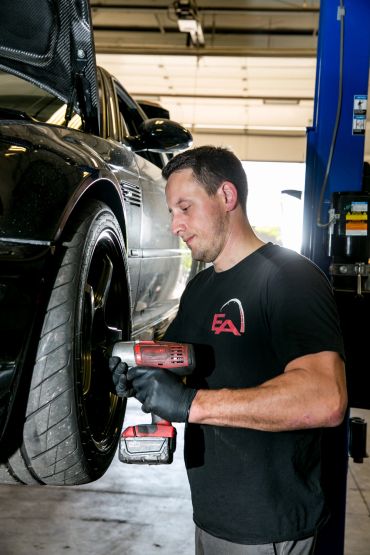 Mechanic tightening car wheel bolts with power tool.