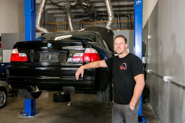 Man standing next to a black BMW on a car lift.