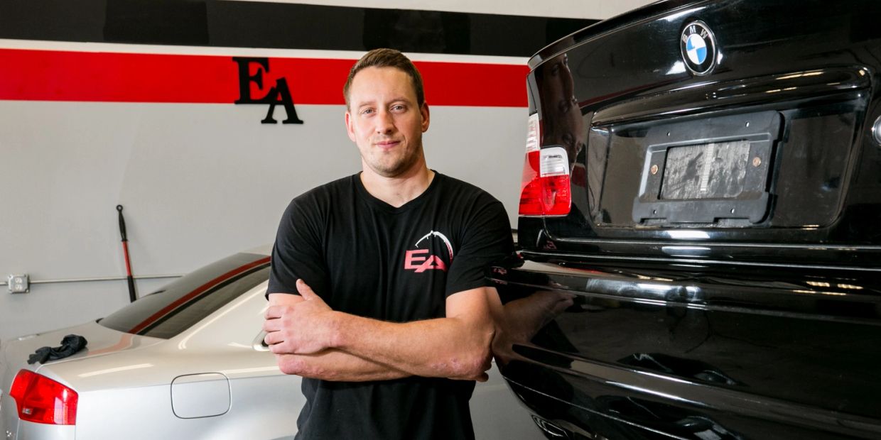 Man standing between a white and black car in a garage.