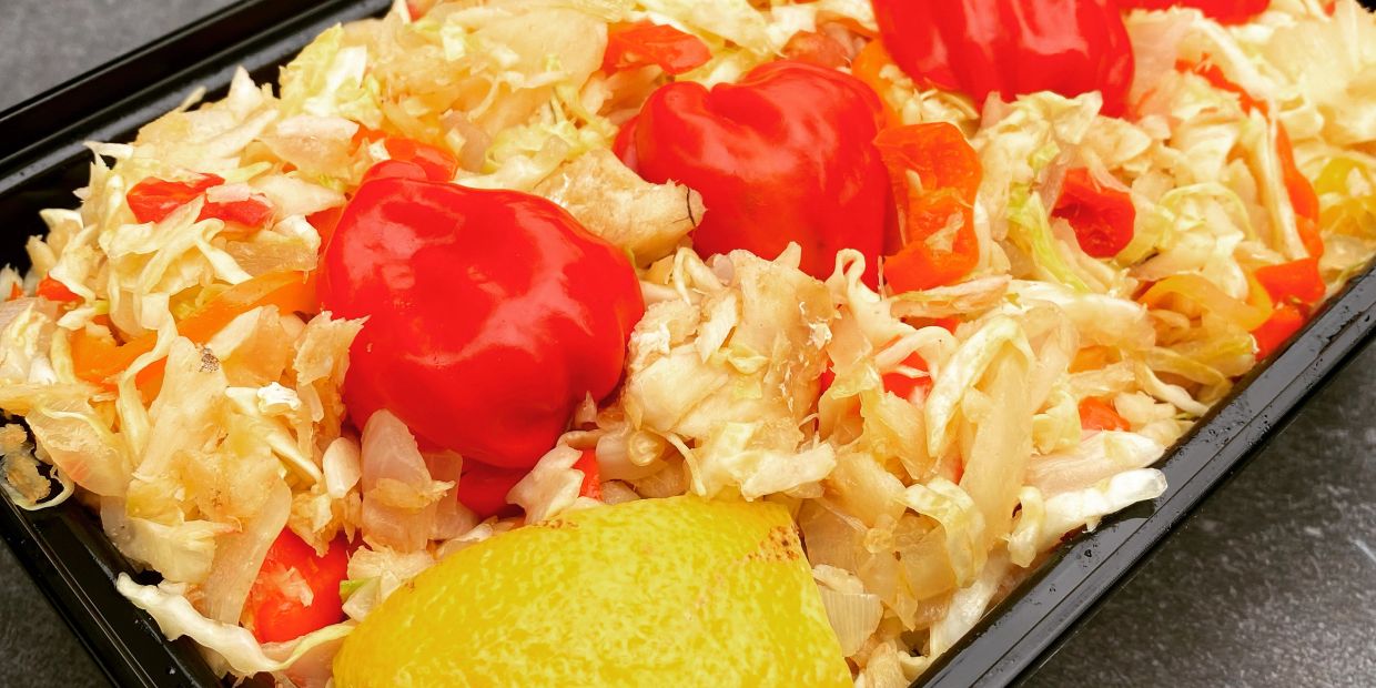 A dish with chopped vegetables, red peppers, and a lemon slice.