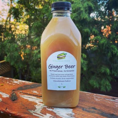 A bottle of homemade ginger beer on a wooden surface outdoors.