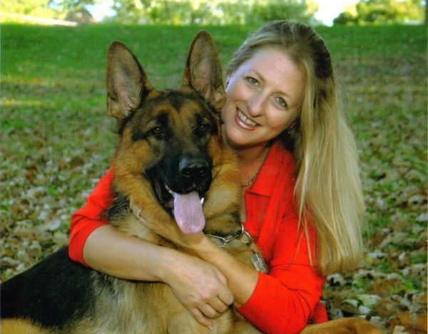 Woman in red hugging a happy German Shepherd outdoors.