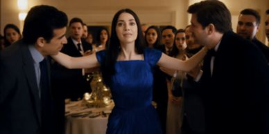 Woman in blue dress with arms extended between two men in suits at a formal event.