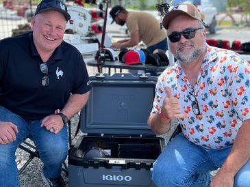 Two men smiling beside an open Igloo cooler outdoors.