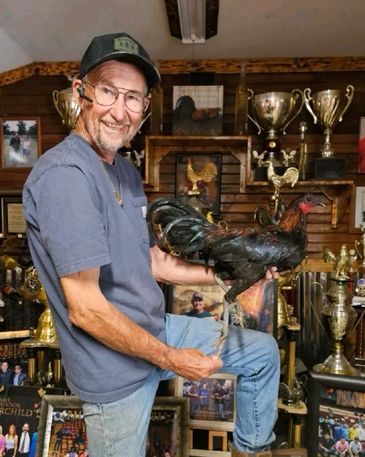 Man proudly holding a rooster in a trophy-filled room.