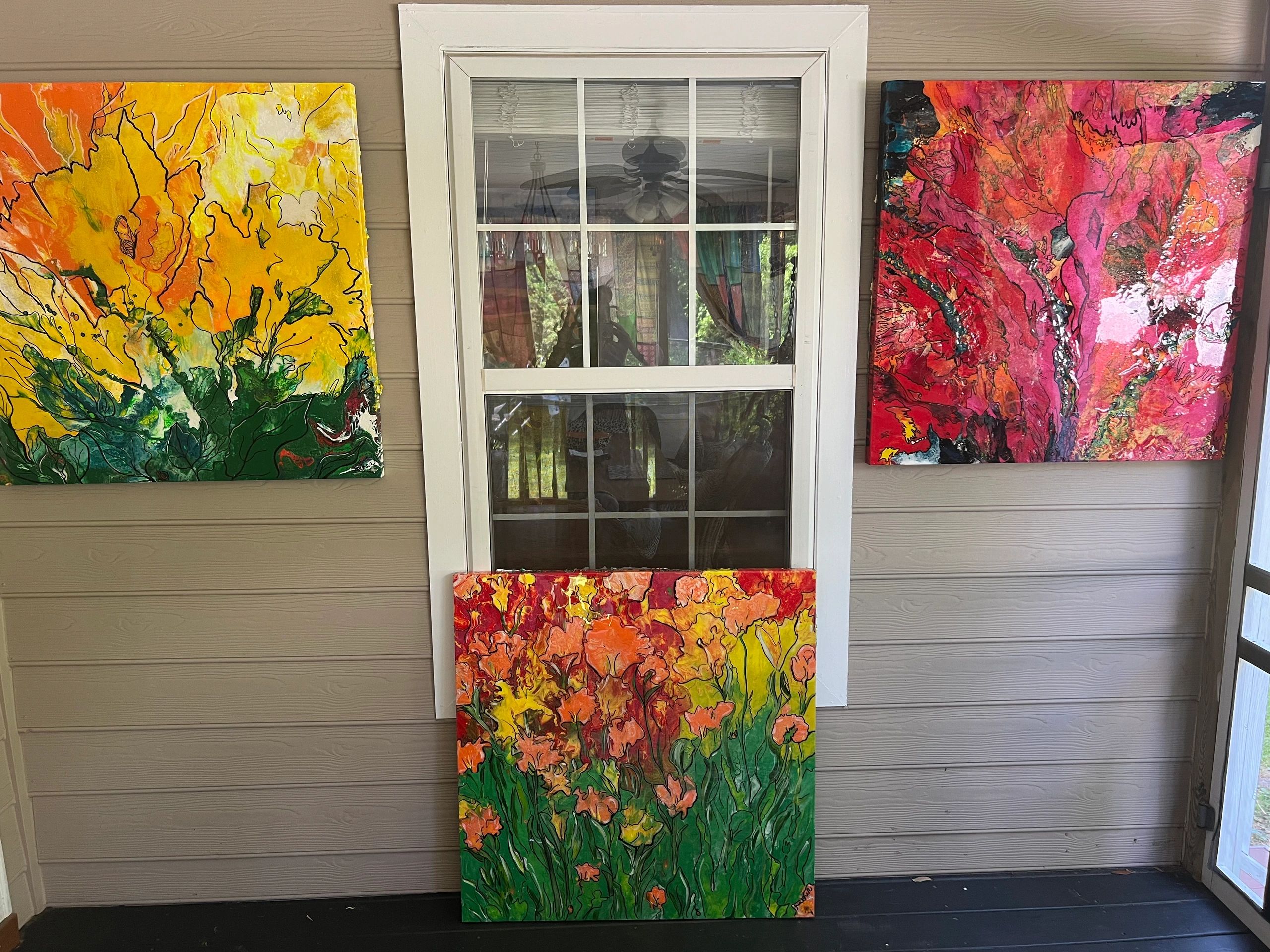 Three colorful floral paintings displayed around a white window.