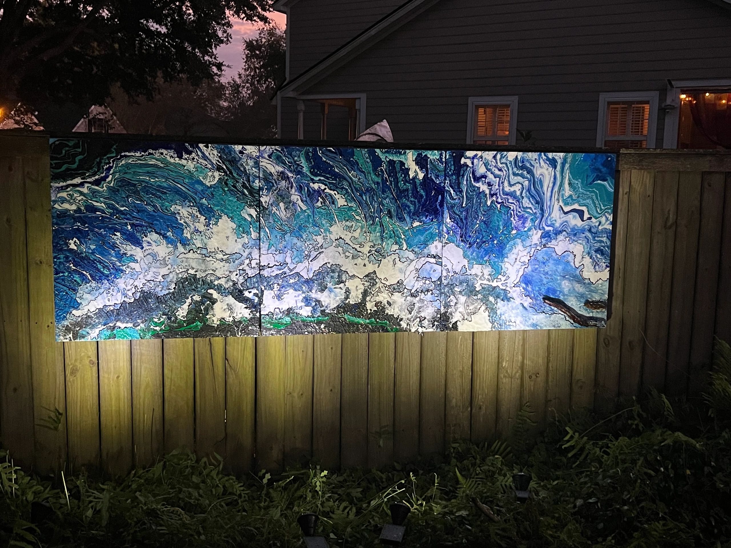 Abstract blue and white painting on a wooden fence at night.