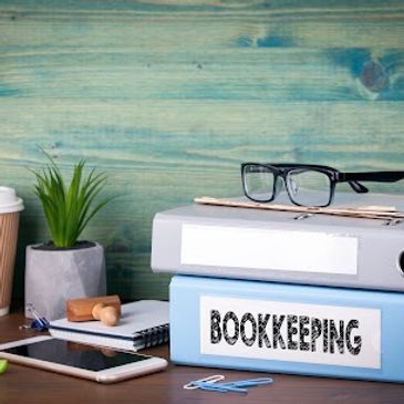 Desk setup with a coffee cup, plant, glasses, and bookkeeping binders.