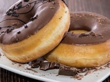 Two chocolate-glazed donuts on a white plate with chocolate shavings.