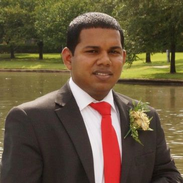 Man in suit with red tie near a park water body.