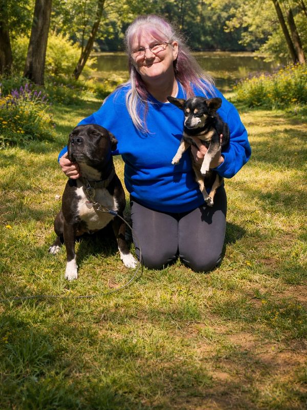 Woman kneeling outdoors with two dogs, smiling in the sunshine.