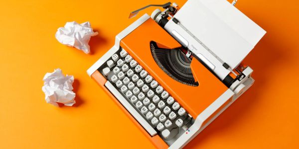 Orange typewriter with crumpled paper balls on an orange background.