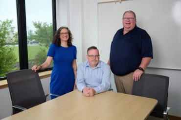 Three people posing in a conference room.