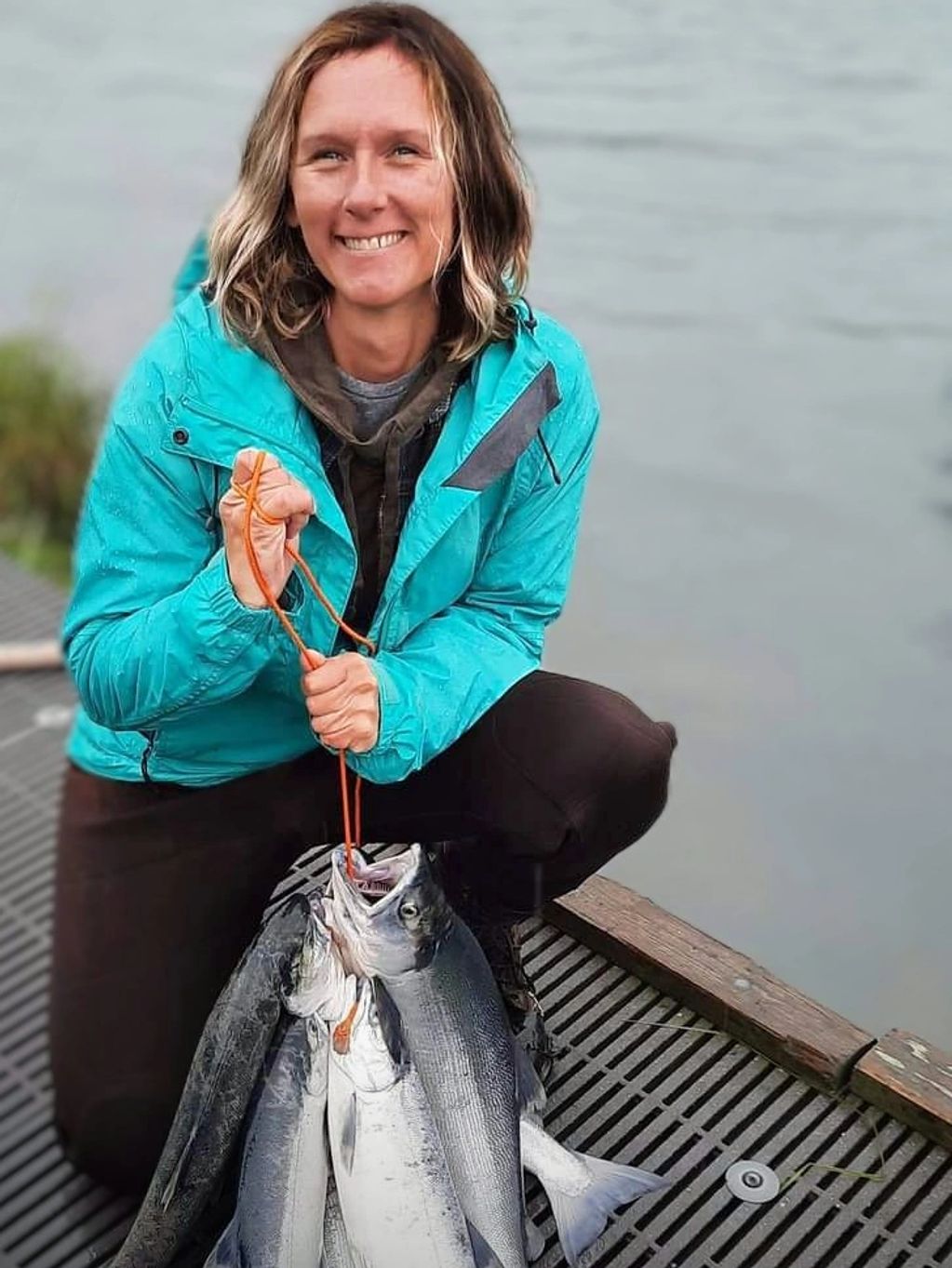 Woman proudly holding freshly caught fish by the water.