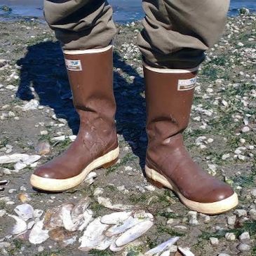 Person wearing brown rubber boots standing on a rocky shore.