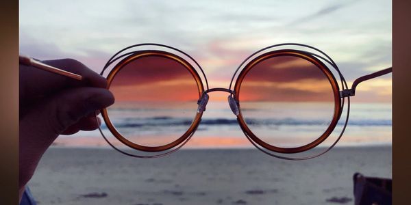 Sunset viewed through round sunglasses on a beach.