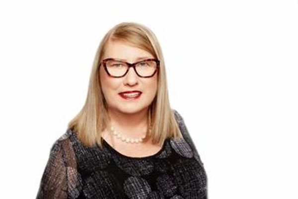 Karen McDonald, a blonde professional in a black top with glasses looks at the camera and smiles