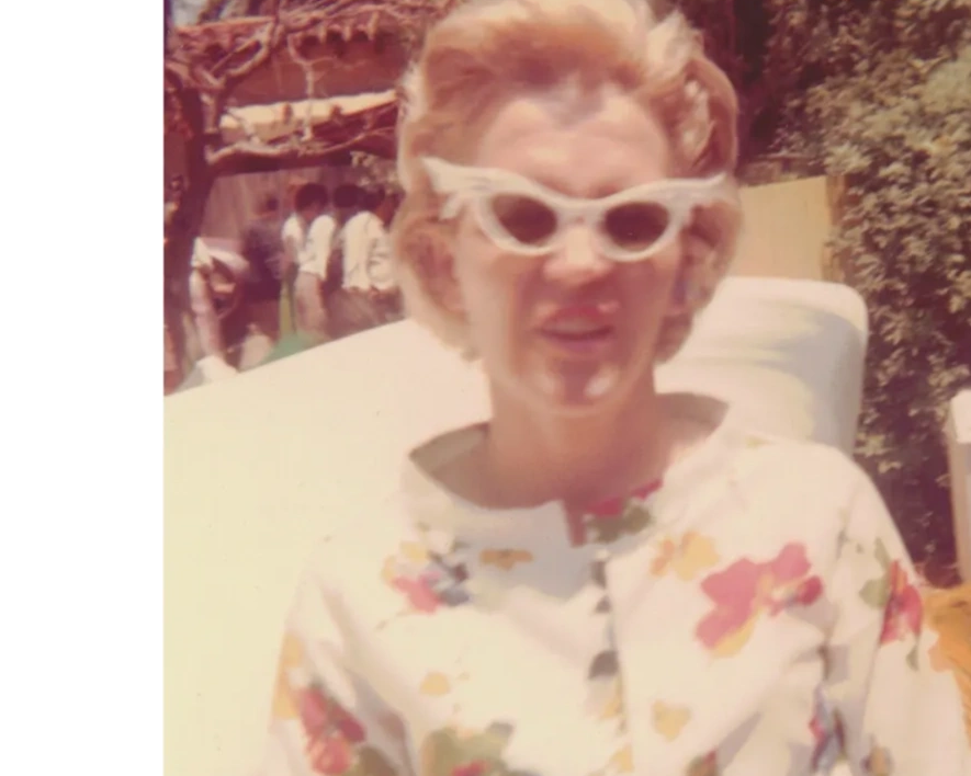 Woman in vintage floral dress and cat-eye sunglasses outdoors.