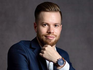 young man dressed in smart blue suit holding hand under his chin