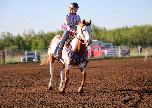 A young girl rides a horse in an outdoor arena, wearing a helmet and colorful outfit.