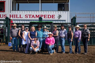 Group photo at a rodeo event with a 'Stampede' sign.