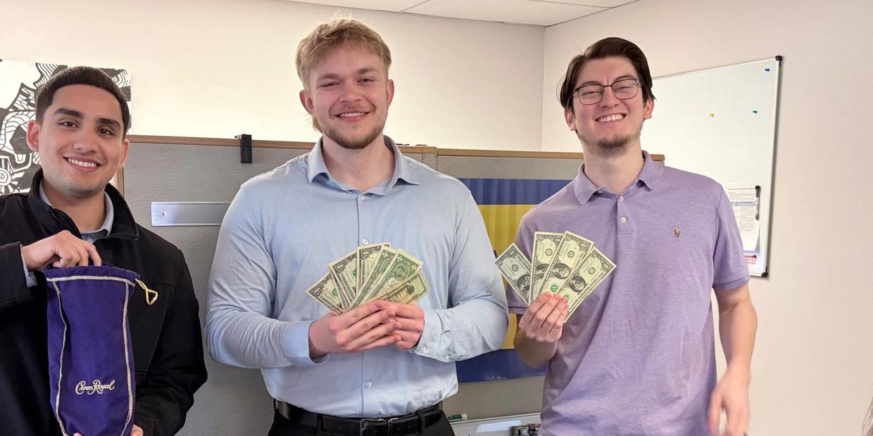 Three smiling men holding cash and a purple Crown Royal bag indoors.