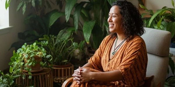 A woman in an orange dress sits peacefully surrounded by lush green plants.