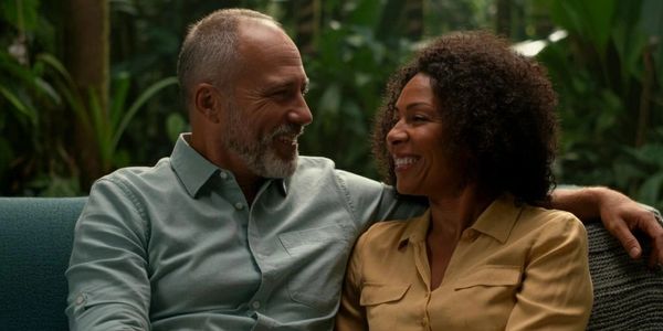 A happy mature couple sitting close and smiling on a couch surrounded by greenery.