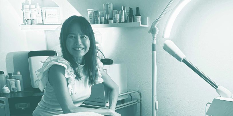 Smiling woman in a skincare treatment room with bright medical light.