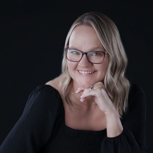Smiling woman with glasses in a black top against dark background.