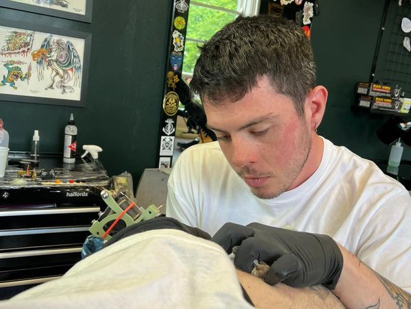 Matt King doing his first tattoo, in a tattoop shop - a traditional skull tattoo