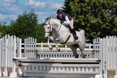 Rider and white horse jumping over a fence in an equestrian event.