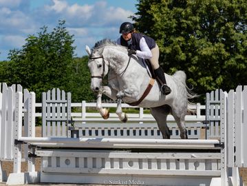 Person on white horse jumping over obstacle in competition.