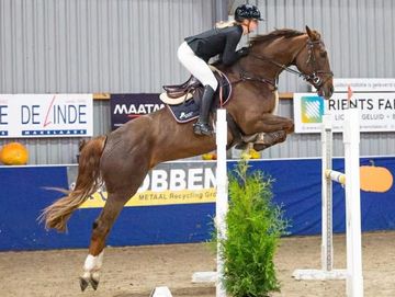 A rider jumps a horse over a hurdle indoors.