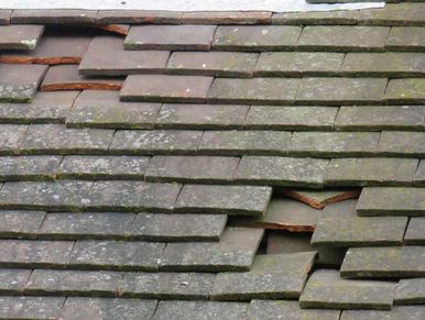 A close-up of damaged roof tiles with visible gaps and moss.