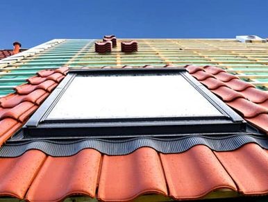 Partially tiled roof with a skylight under clear blue sky.