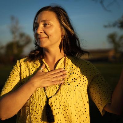 Woman in yellow blouse with hand on chest, basking in golden sunlight.