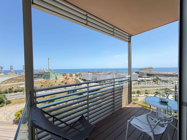 Balcony with modern chairs overlooking a coastal industrial area and sea.